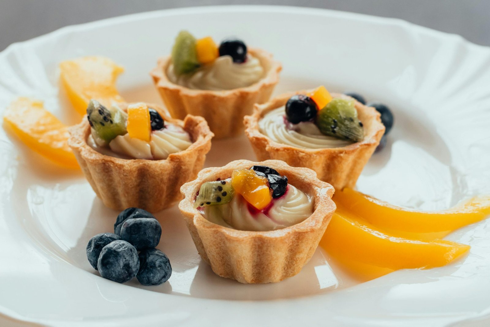Close-up of fruit tarts topped with fresh berries and kiwi on a white plate.